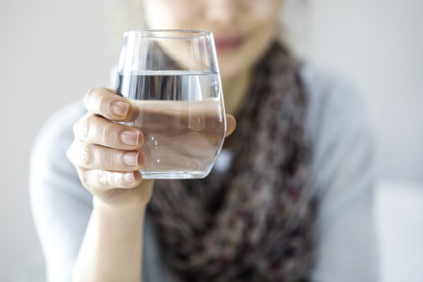 Woman holds glass of water to stay hydrated before colonoscopy.